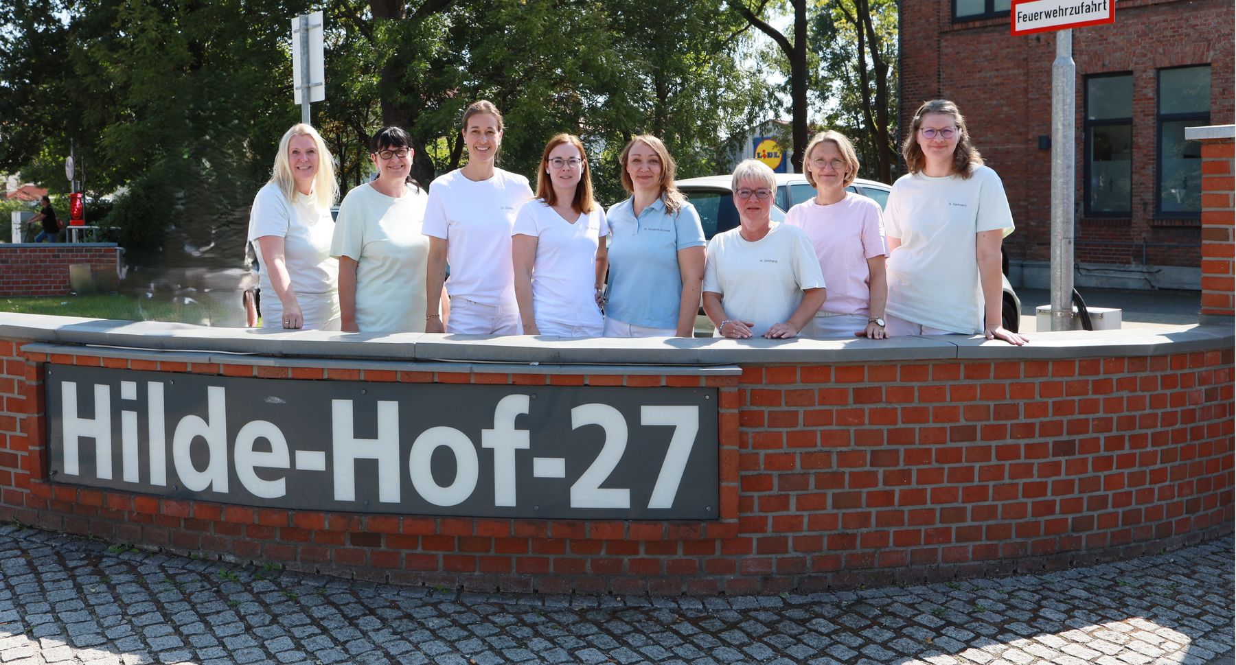 Das Praxisteam sitzt gemeinsam auf der Mauer mit der Aufschrift Hilde-Hof-27