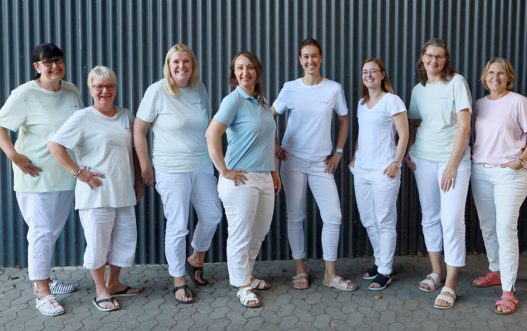 Das gesamte Praxisteam in hellen Praxisshirts vor einer Wand